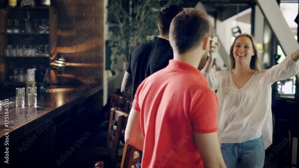 Image of young men in casual dress sitting in the cafe at bar counter. Handsome fellows sitting at the table standing up and welcoming their arrived female friends embracing and kissing them warmly. Image of young men in casual dress sitting in the cafe at bar counter. Handsome fellows sitting at the table standing up and welcoming their arrived female friends embracing and kissing them warmly.