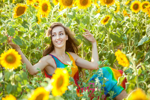 Happy and lovely woman sits in a field among yellow sunflowers. photo