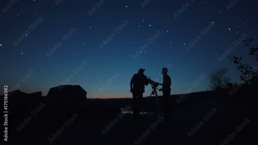 Black silhouettes of people looking through telescope on stars in dark twilight on shore.