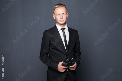 Businessman in suit looking through binoculars in hands with gray background photo