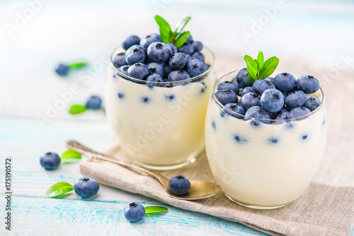 Clear jar of yogurt with blueberries over on wooden background