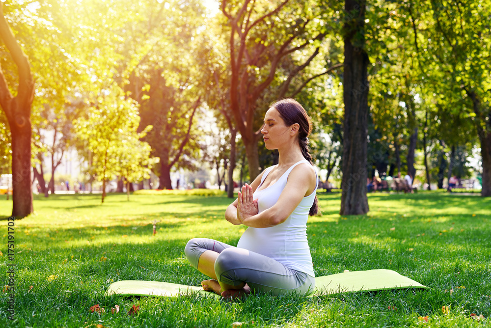 Adorable pregnant woman sitting in lotus pose and relaxing in park Adorable pregnant woman sitting in lotus pose and relaxing in park