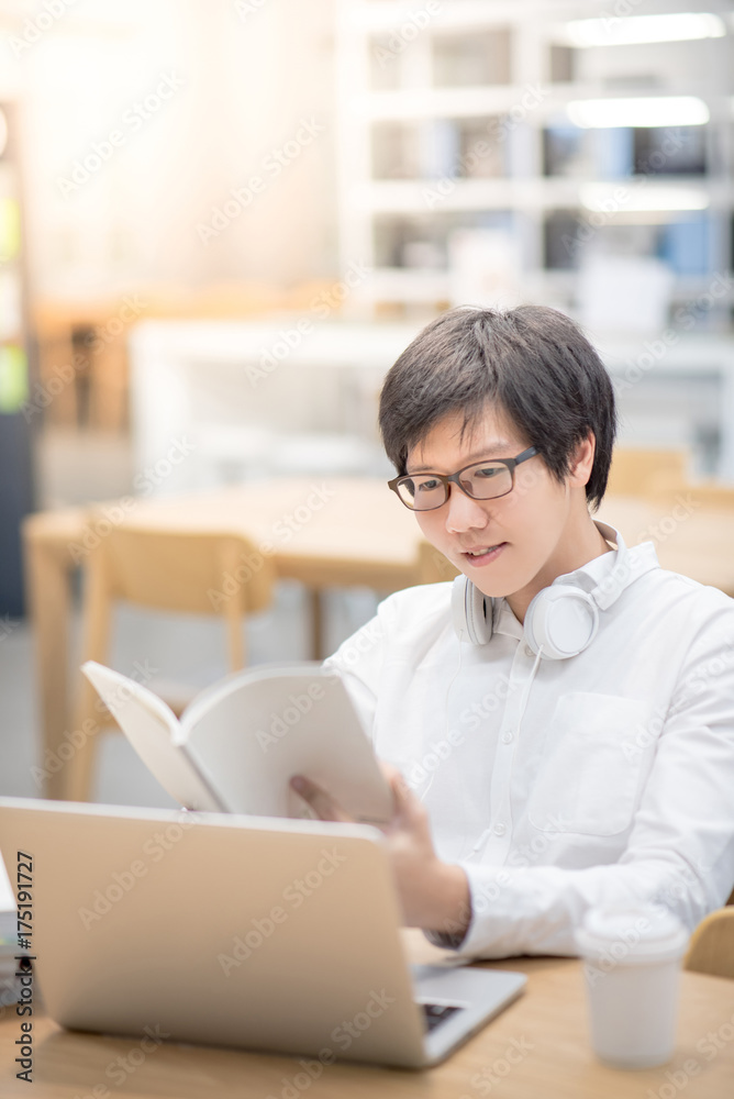 Young Asian man university student smiling and reading book in library, education research and self learning in college life concepts