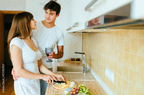 Young couple in kitchen in the morning, hispanic woman and european man hug drink tea and cooking breakfast in modern apartment interior. Real people concept.