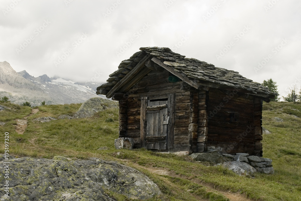 Panorama: Close-up of a typical mountain Hut / Cabin, made of old hardwood and roof with stone slabs, in the background Belalp mountains, late summer, clouds, switzerland Panorama: Close-up of a typical mountain Hut / Cabin, made of old hardwood and roof with stone slabs, in the background Belalp mountains, late summer, clouds, switzerland