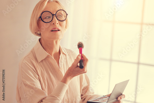 Aged pleasant woman apllying dry concealer on her face photo