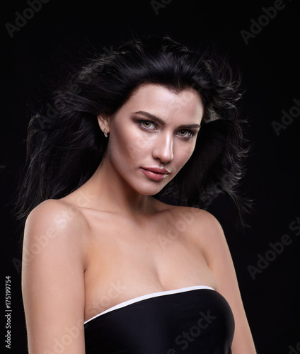 Portrait of a young brunette woman with long black streaming hair on black