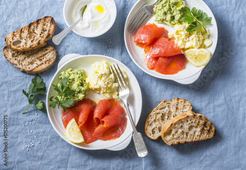 Two plates of breakfast or snack - egg salad, salmon and avocado puree on a blue background, top view. Healthy food concept