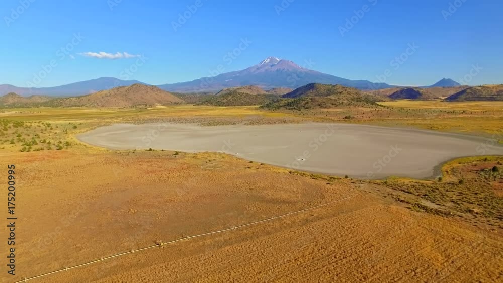 Cinematic, sweeping camera motion of a warm and colorful dry lake bed with rock formation, revealing farmland on pasture lands and hills of iconic northwest landscape with Mt Shasta and Mt Black Butte Cinematic, sweeping camera motion of a warm and colorful dry lake bed with rock formation, revealing farmland on pasture lands and hills of iconic northwest landscape with Mt Shasta and Mt Black Butte