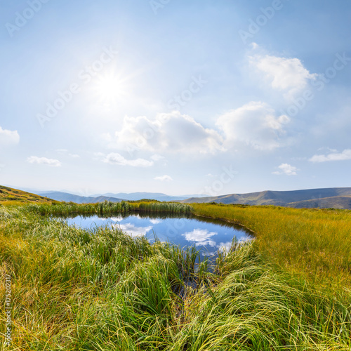 small lake among a hills near a sparkle sun