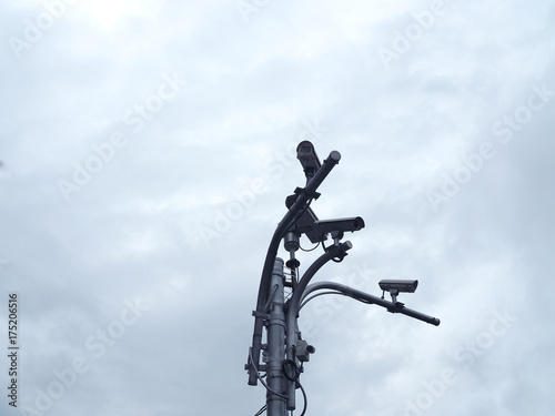 Grey metal steel pole bundled with many CCTV camera aim for vary view of traffic street below, with cloudy dark sky background