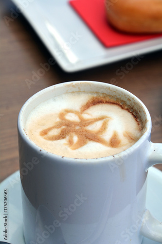 Cup of foamy cappuccino on a plate on a wooden table.