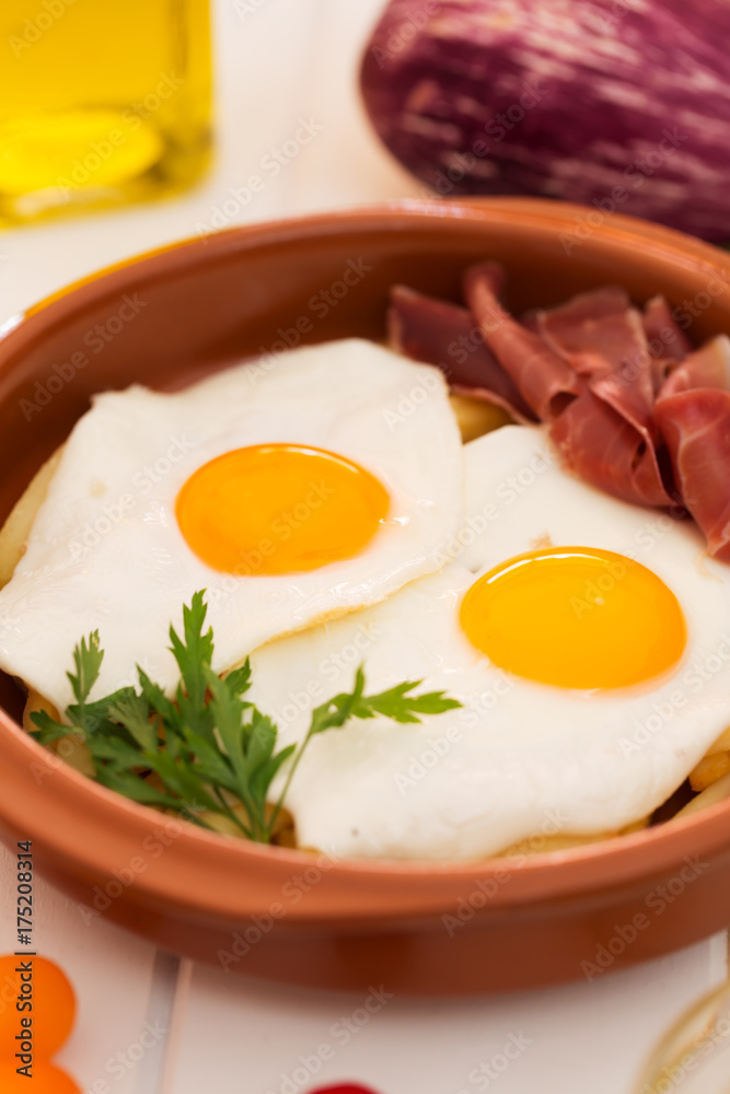 Fried eggs in a ceramic cup with spanish jamon for breakfast on a white background. Close up Fried eggs in a ceramic cup with spanish jamon for breakfast on a white background. Close up