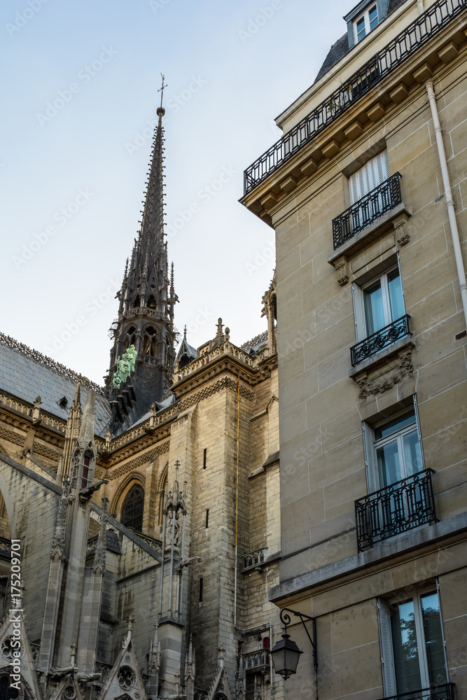 Low angle view of the spire of Notre-Dame de Paris cathedral at sunset with a residential building in the foreground.