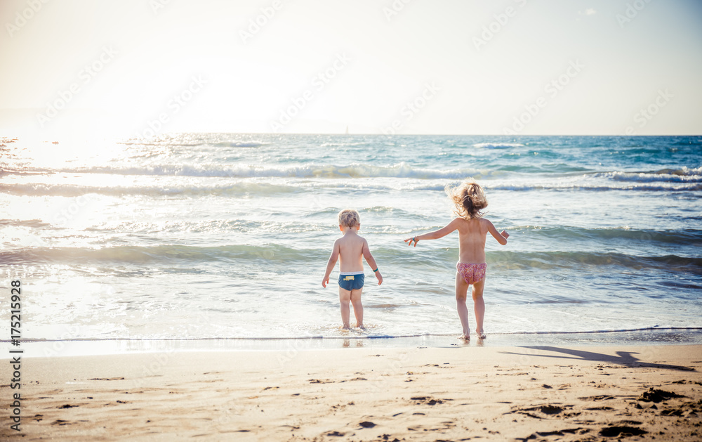 two kids play with wave on summer beach