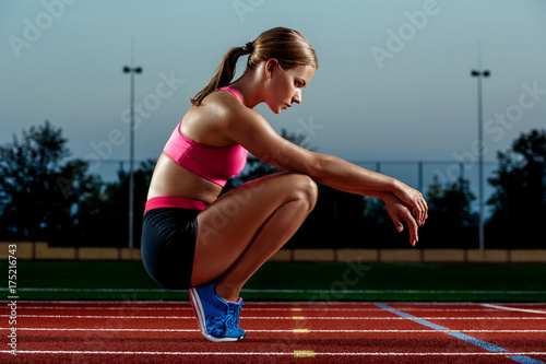 Picture of beautiful young European female runner or sprinter sitting on outdoor stadium track, feeling exhausted after sprint or marathon.