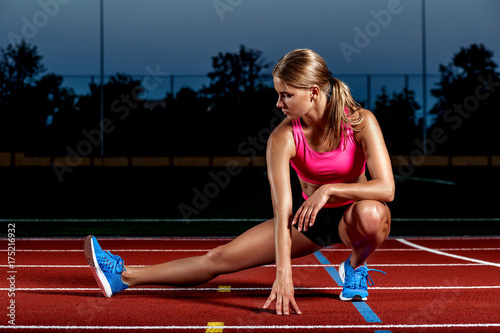 Attractive young woman athlete stretching legs on stadium