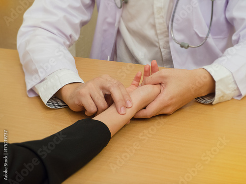 Close up the hand ofThe human in white uniform,Doctor is working,by finger pressing on the patient arm for checking heart rate ,vintage tone,blurry light background.