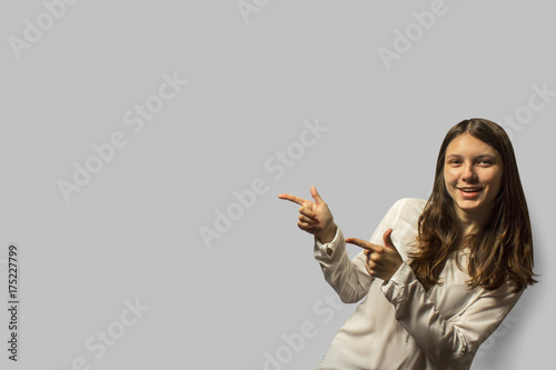 portrait of a young beautiful student girl with long hair. smiling and Pointing by fingers of both hands toward the space for text. concept of recomendations. isolated on a gray background.