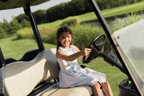 A little girl is sitting in the driver's seat in the golf car