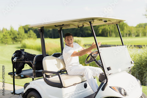 Happy man on a white golf cart looking into the camera and showing a hand forward