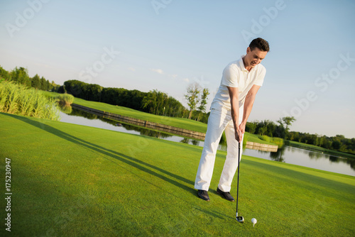A man is standing on a golf course and getting ready to hit the ball with a golf club