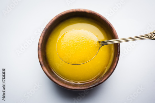 Ghee or clarified butter close up in wooden bowl and silver spoon, selective focus
