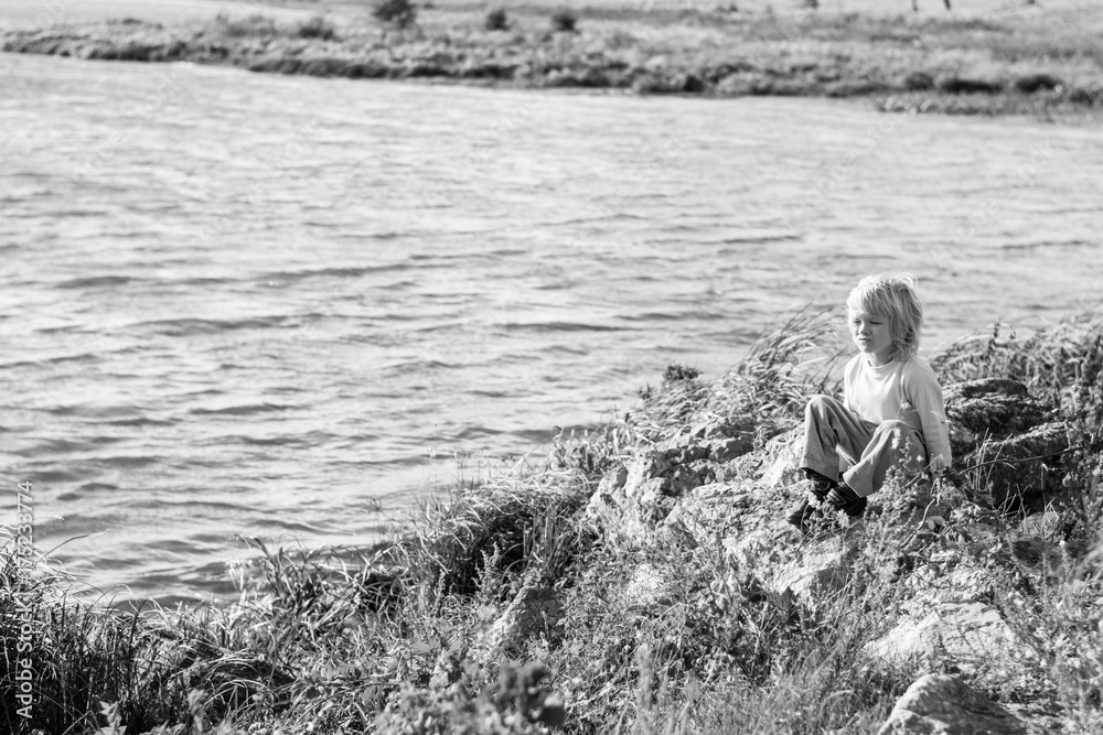 Blond thoughtful boy sitting at a river bank on a rocks - Rusiian Urals wind sunny day - black and white photo