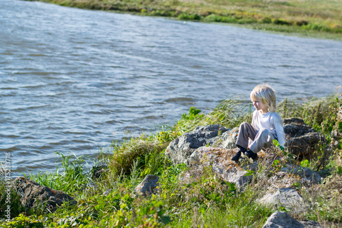 Obraz na płótnie Blond thoughtful boy sitting at a river bank on a rocks - Rusiian Urals wind sunny day w salonie