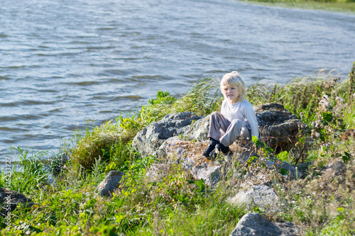 Obraz na płótnie Blond thoughtful boy sitting at a river bank on a rocks - Rusiian Urals wind sunny day w salonie