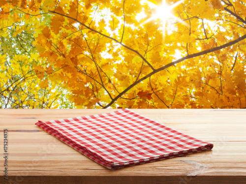 Empty wooden deck table with tablecloth over bokeh autumn leaves background. Kitchen background, product montage display. Mock up .