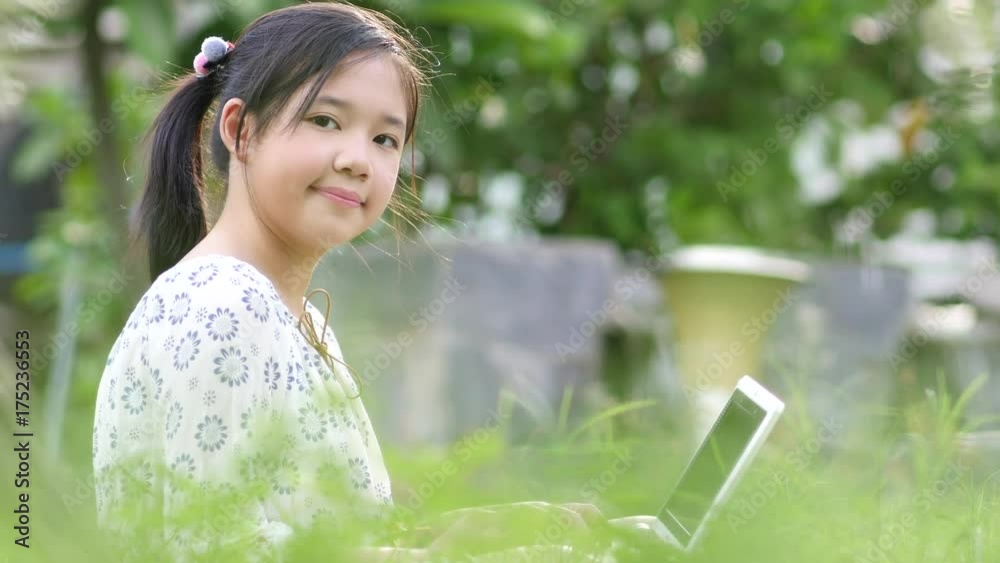 Beautiful Asian girl sitting in park on the green grass with laptop Beautiful Asian girl sitting in park on the green grass with laptop