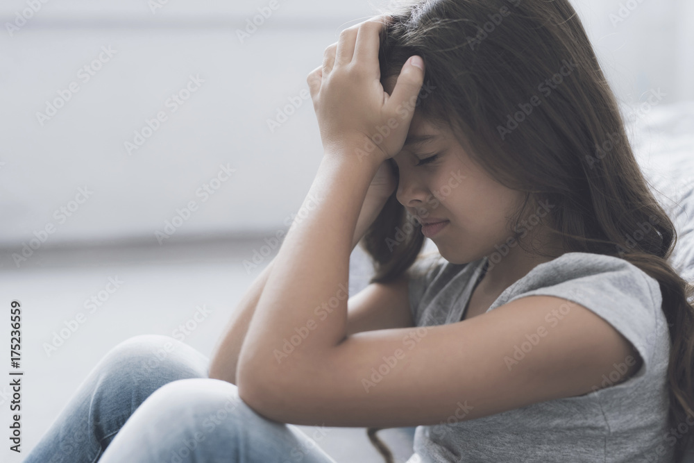 Little dark-haired girl sits and cries holding her head in her hands Little dark-haired girl sits and cries holding her head in her hands