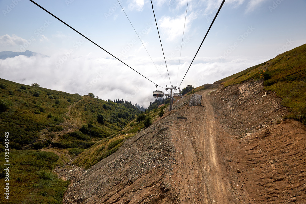 Naklejka premium View from top of ropeway with multiple seats and stretched cables above trees in deep fog. Mountains of the North Caucasus.
