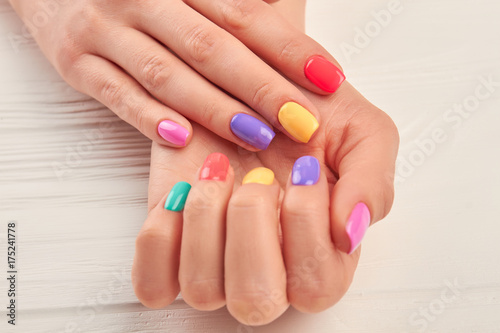 Female hands with stylish summer manicure. Woman hands with colorful nail polish close up. Well-groomed hands with bright manicure on wooden background.