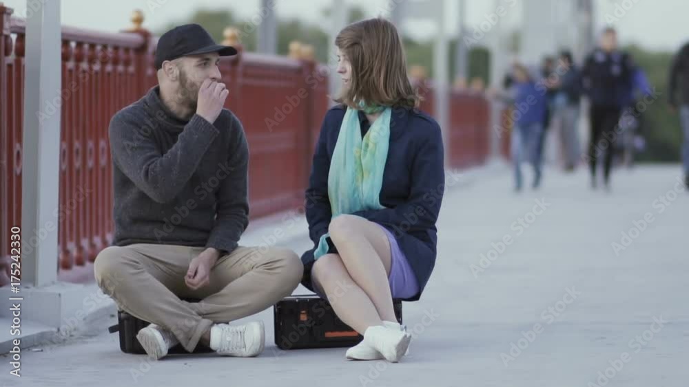 Friends sitting on suitcases on the bridge and talking Friends sitting on suitcases on the bridge and talking