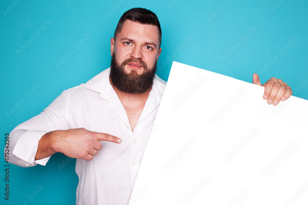 handsome young man with long beard and moustache on face with pointing finger on blue background in studio, copy space handsome young man with long beard and moustache on face with pointing finger on blue background in studio, copy space