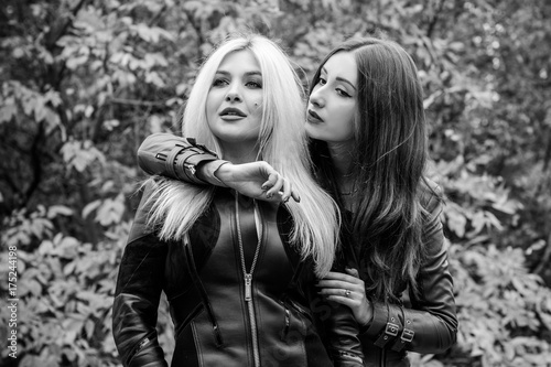 Two beautiful ladies at autumn forest in leather jackets. Mutual relations of women, girlfriends. All about women and their psychology