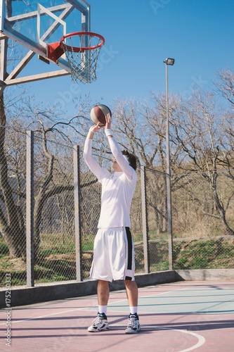 Portrait of a basketball player walking on an outdoor basketball court and dribbling the ball © sashafolly