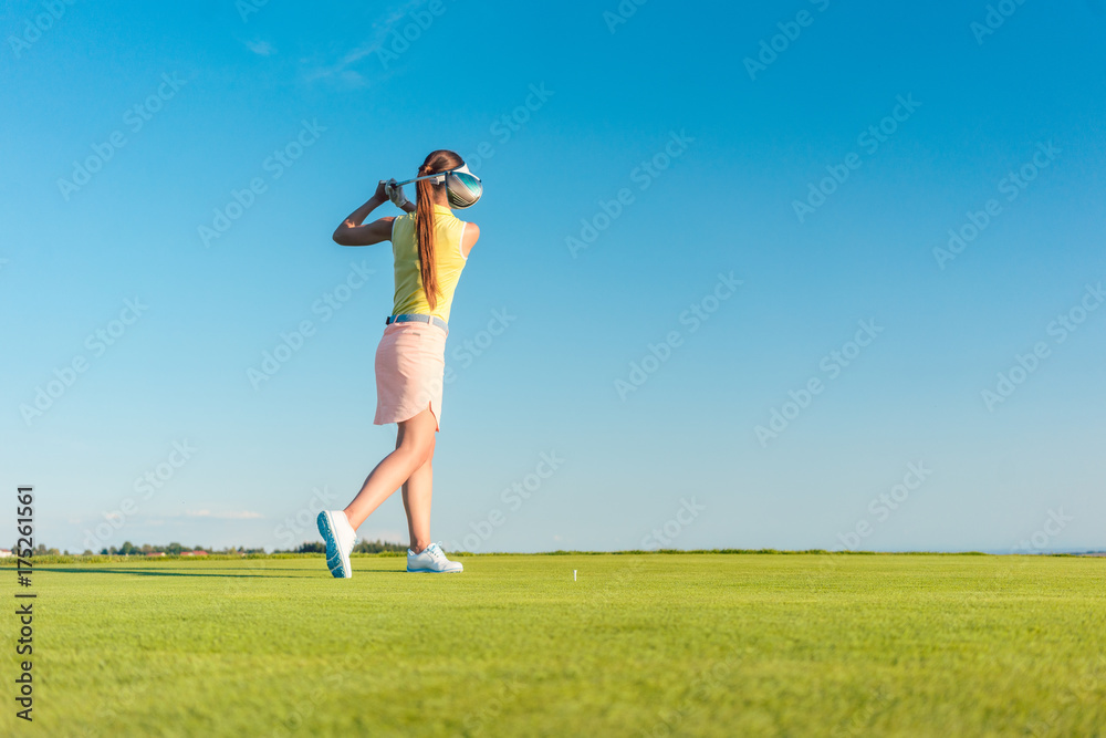 Full length of a professional female golf player smiling while swinging a driver club with concentration and accuracy before hitting the ball during individual practice Full length of a professional female golf player smiling while swinging a driver club with concentration and accuracy before hitting the ball during individual practice
