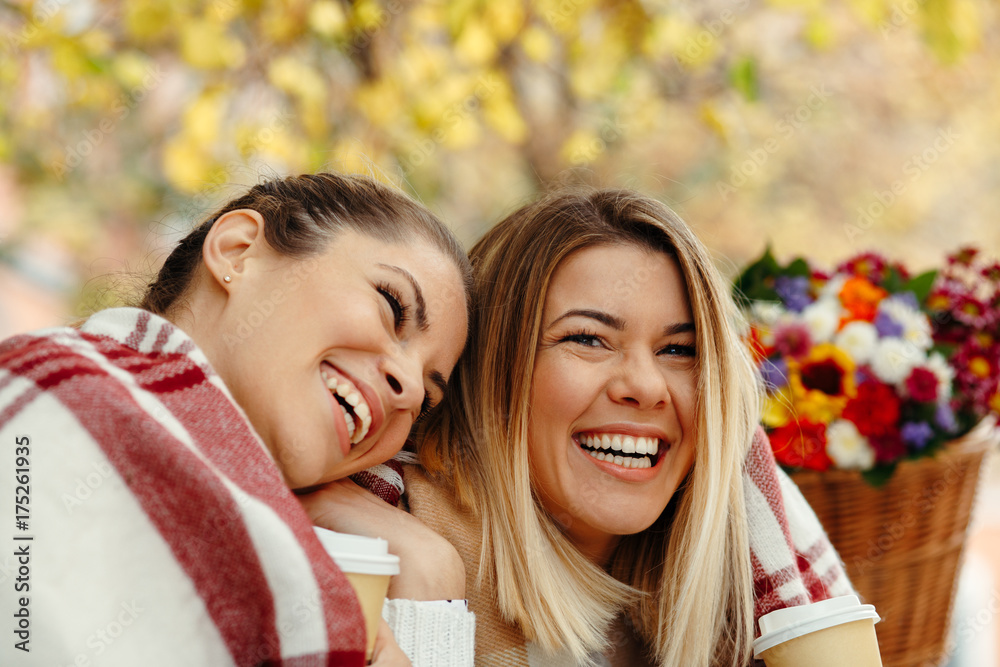 Obraz premium Two women smiling and laughing with a blanket on a bench enjoying coffee