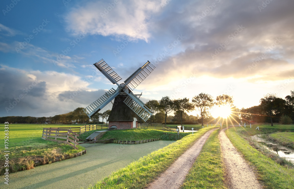 Obraz premium windmill, rural road and river at sunrise