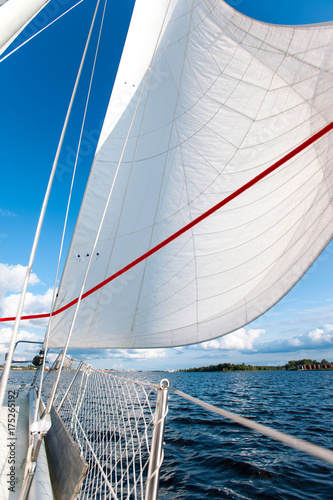 White yacht sails in sunlight on blue cloudy sky background.