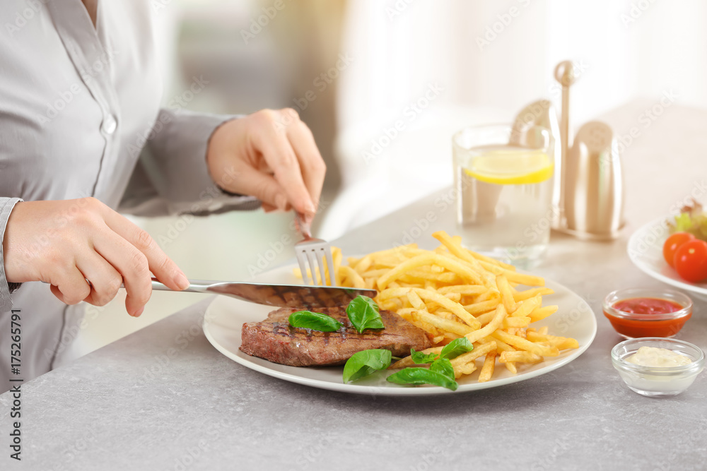 Woman eating delicious grilled steak with fries in restaurant