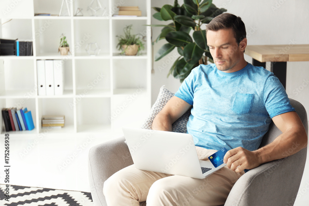 Young man holding credit card while using laptop at home Young man holding credit card while using laptop at home