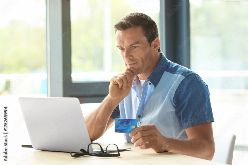 Young man holding credit card while using laptop at home