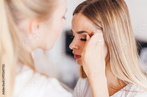 Professional makeup artist working with beautiful young woman in white T-shirt with word "less"