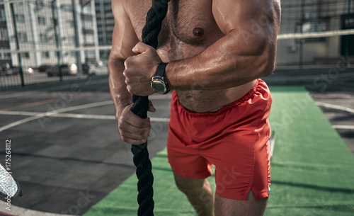 Close-up. Athletic man pulling the rope. Sport equipment. Outdoors. Green colors. Sports ground.