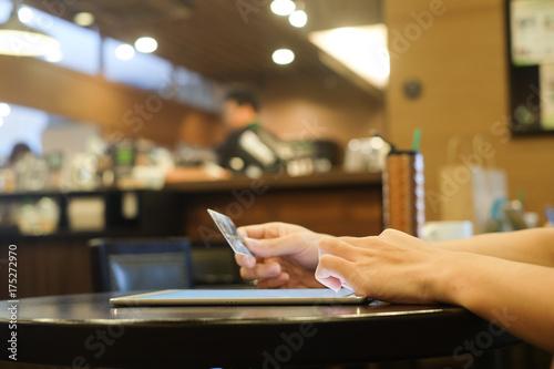 close up man hand touch screen on tablet pad and holding credit card for shop online in coffee restaurant