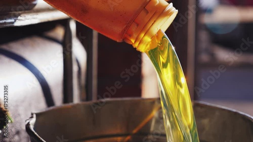 Worker pours engine oil or chemical liquid into the metal bucket